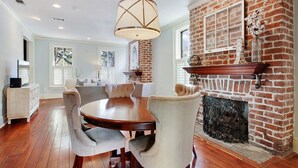 A dining area with a brick fireplace, a round wooden table, and white upholstered chairs. - Historic 2 Story Home w/ Balcony, Parking on Calhoun Square by Lucky Savannah (Savannah)