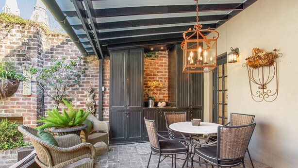 An outdoor patio with wicker furniture, a brick wall, and a hanging lantern. - Historic 2 Story Home w/ Balcony, Parking on Calhoun Square by Lucky Savannah (Savannah)