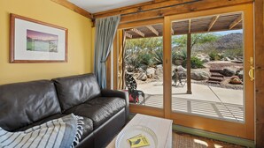 A room with a leather sofa, a framed picture on the wall, and a view of an outdoor patio with desert plants and rocks.