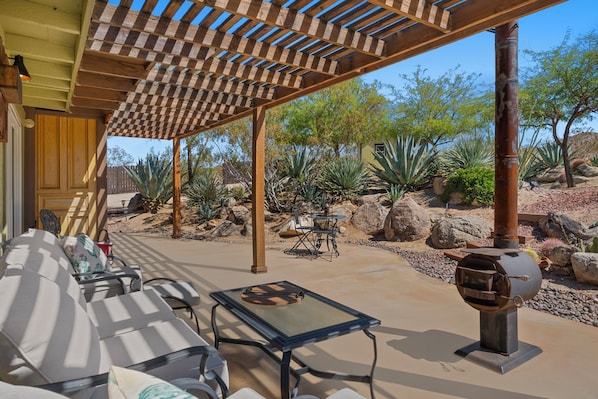 An outdoor patio with a wooden pergola, a glass table, and a grill.