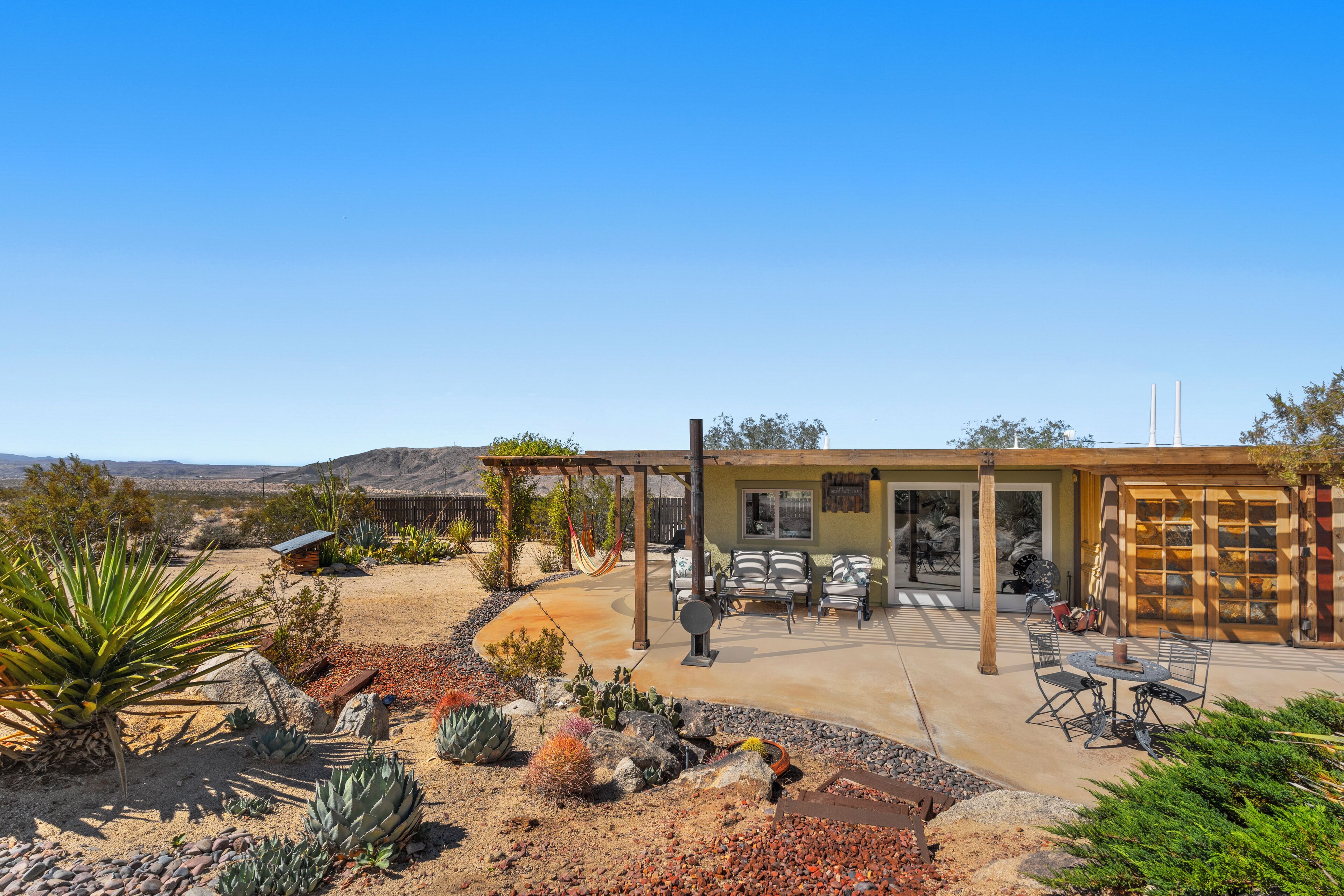 Un patio al estilo desértico con una pérgola, asientos exteriores y vistas del paisaje circundante.
