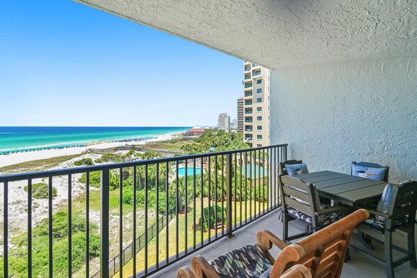 A balcony with a view of a beach, a pool, and a building in the background.