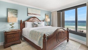 A bedroom with a large bed, a nightstand, a lamp, and a view of the ocean. - Beach Front Balcony ~ Seasonally Heated Pool (Miramar Beach)