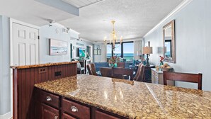 A kitchen with granite countertops, wooden cabinets, a chandelier, and a view to the outside. - Beach Front Balcony ~ Seasonally Heated Pool (Miramar Beach)