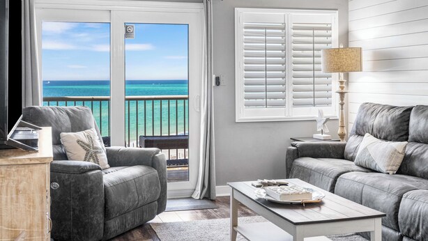 A living room with a grey sofa, a coffee table, and a TV on a stand. There is a balcony with a view of the ocean. - 620- Time for a trip to the Beach? Rustic, Coastal Beachfront Retreat (Destin)