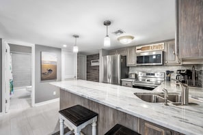 A modern kitchen with a large island, stainless steel appliances, and a view of the beach through the window.