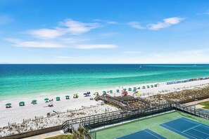 Una playa con cancha de tenis, sombrillas y un paseo marítimo.