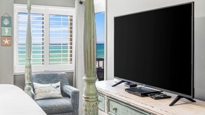 A room with a large flat-screen TV on a wooden cabinet, a chair with a cushion, a decorative pillar, and a window with a view of the ocean. - 620- Time for a trip to the Beach? Rustic, Coastal Beachfront Retreat (Destin)