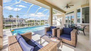 A covered outdoor area with wicker furniture, a pool, and a view of a residential area. - Waterfront Home | Pool, Spa & Walk to Beach (Marco Island)
