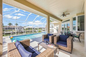 A covered outdoor area with wicker furniture, a pool, and a view of a residential area.