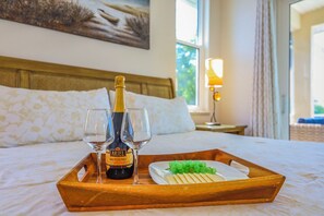 A wooden tray with a bottle of Ariel Brut Cuvée wine, two glasses, and a plate of cheese and grapes on a bed.
