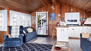 A cozy cabin interior with a living room, kitchen, and a door leading outside.
