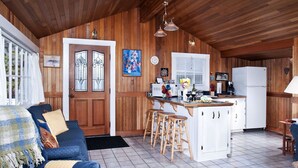 A cozy cabin-style kitchen with wooden walls, a central island with stools, a refrigerator, and a dining area with a table and chairs.