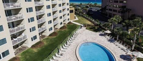 A hotel with multiple balconies, a swimming pool, and a view of the ocean.