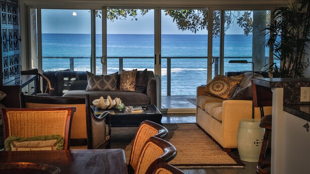 A living room with a view of the ocean, furnished with a sofa, chairs, and a coffee table.