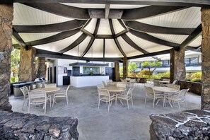 Un patio al aire libre con pilares de piedra, una barra central y varios conjuntos de asientos.