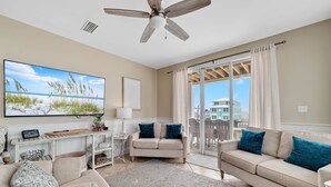 A spacious living room with a large flat-screen TV, a ceiling fan, and a sliding glass door leading to a balcony. - Dream Big by GSVR | Beachview Family Reunion Home w/ Big Pool & Elevator + FREE Activities/Golf (Gulf Shores)