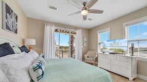 A bedroom with a bed, a ceiling fan, a TV, and a view of the outdoors. - Dream Big by GSVR | Beachview Family Reunion Home w/ Big Pool & Elevator + FREE Activities/Golf (Gulf Shores)
