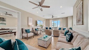 A spacious living room with a beige sofa set, a coffee table, and a ceiling fan. - Dream Big by GSVR | Beachview Family Reunion Home w/ Big Pool & Elevator + FREE Activities/Golf (Gulf Shores)