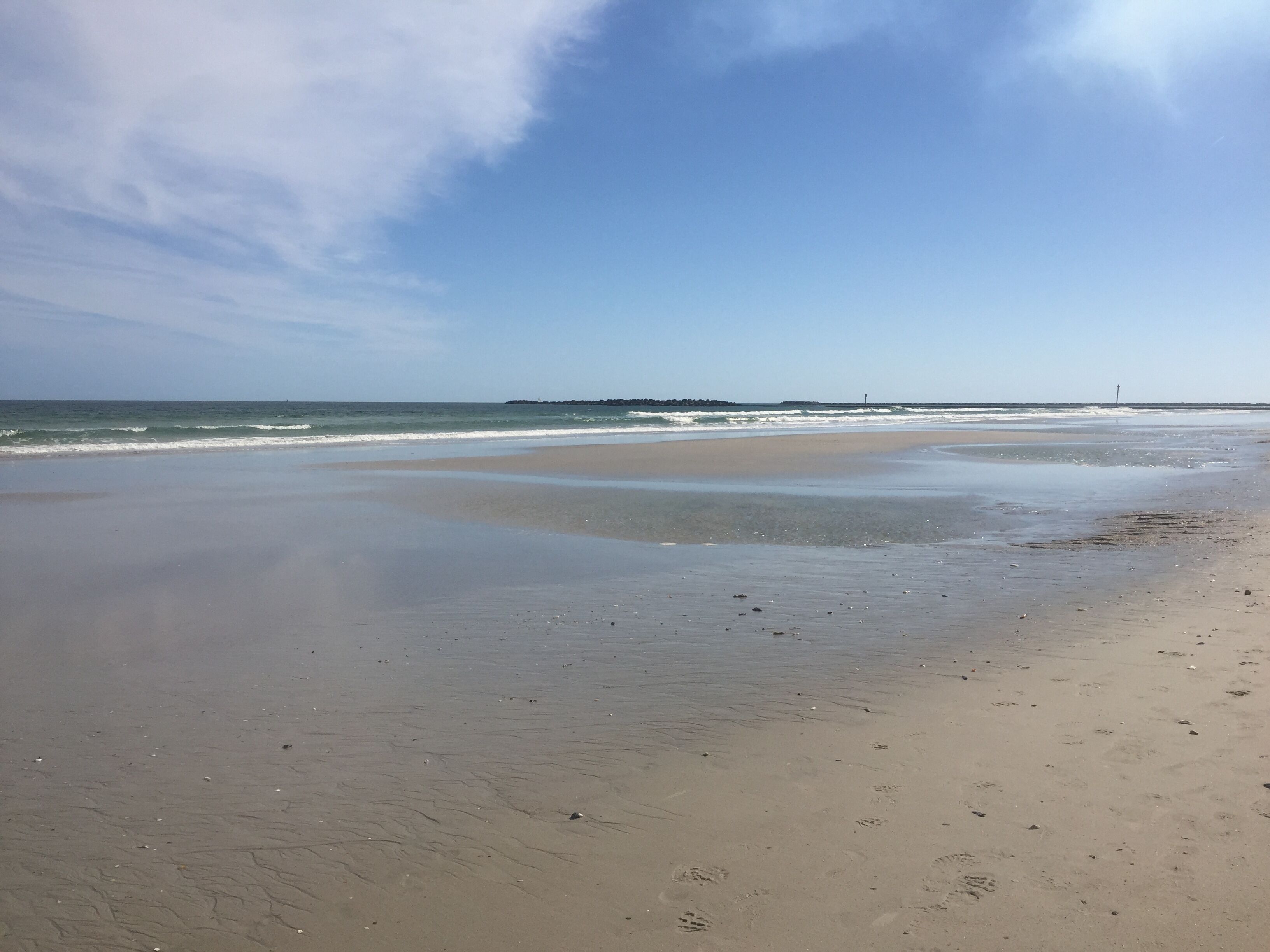 En strand med bred sandstrand, bløde bølger og en klar himmel.