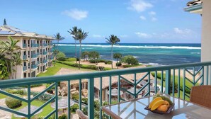 A balcony with a view of the ocean, palm trees, and a building with a tiled roof. - H404 - Ocean View Penthouse Suite with AC - Pool, Hot Tub, & Spa - Walk to shops (Kapaa)