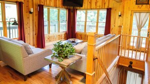 A wooden cabin interior with a sofa, a table with a plant, and a TV mounted on the wall. - Lily Pad - Hosted by The Chalets (Logan)