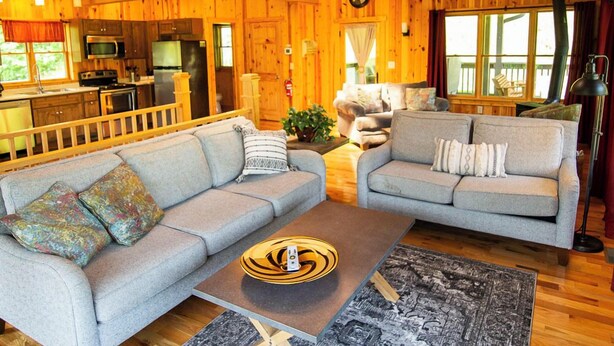 A spacious living area with a sofa, a coffee table, and a dining area with a kitchen. - Lily Pad - Hosted by The Chalets (Logan)