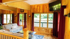 A wooden cabin interior with a sofa, a coffee table, and a TV mounted on the wall. - Lily Pad - Hosted by The Chalets (Logan)