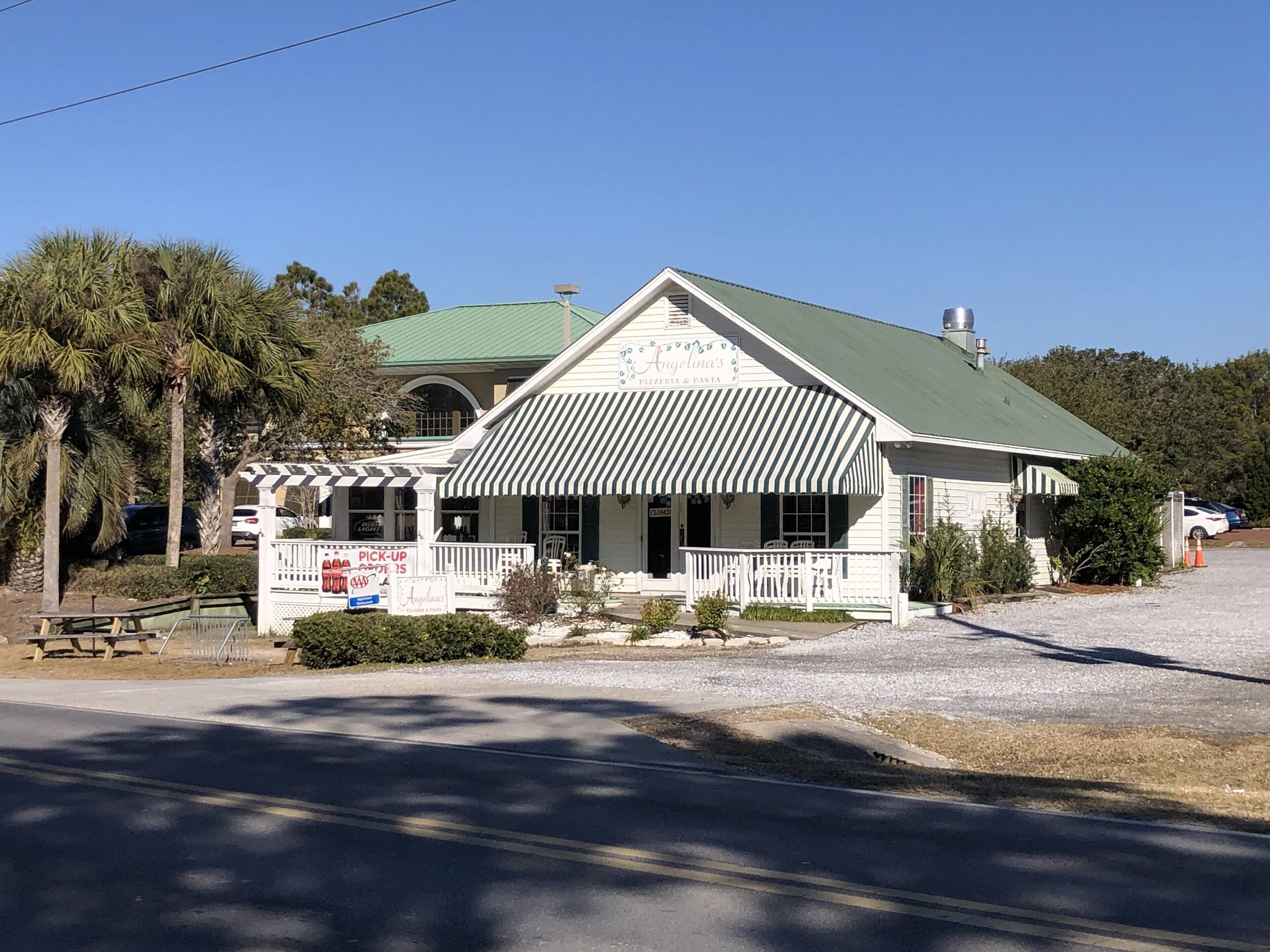 A white building with a green roof and a striped awning, featuring a sign that reads "Angelina's Pizzeria & Pasta."