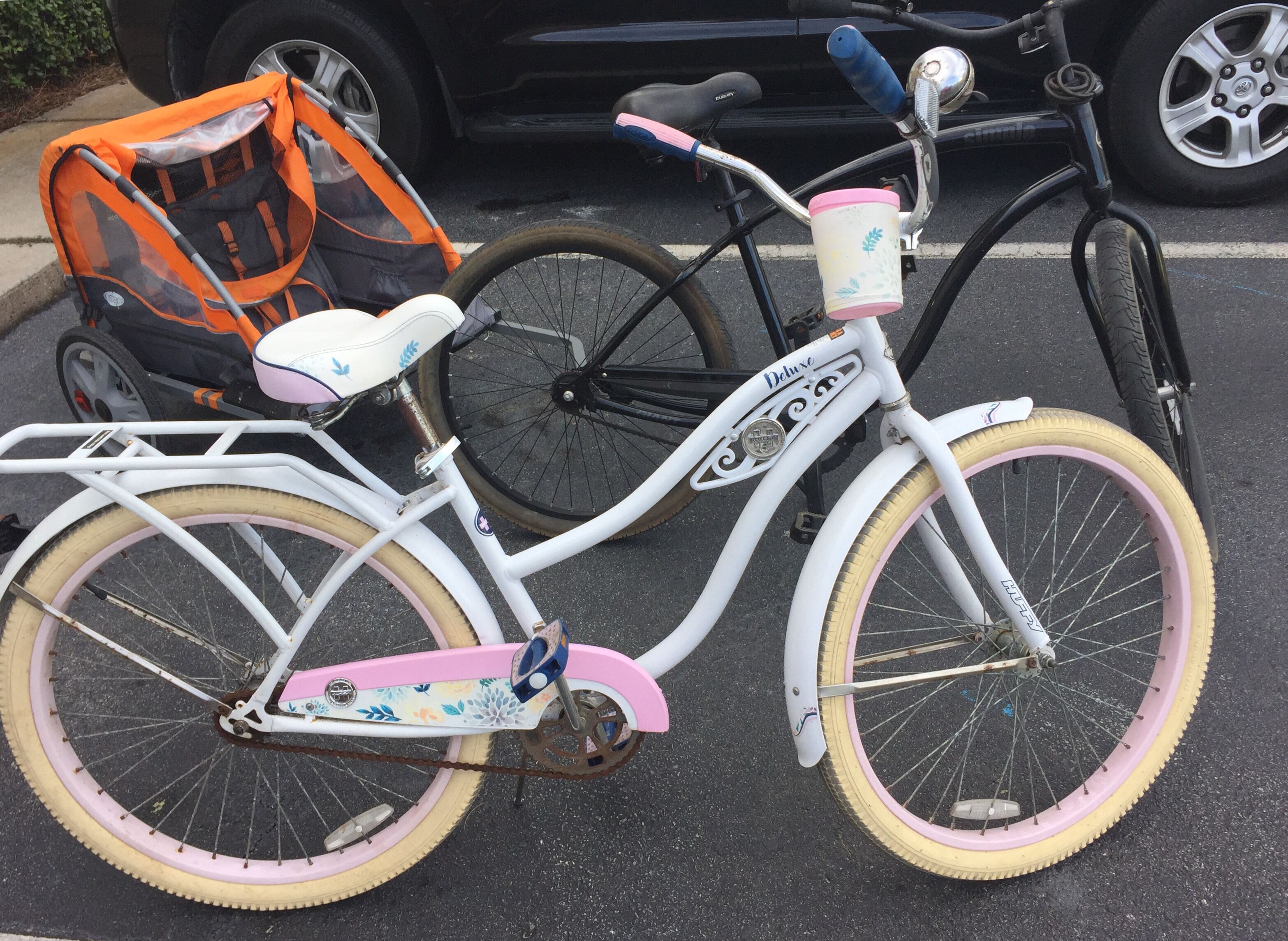 A white bicycle with pink accents and a floral design, parked in a parking lot.