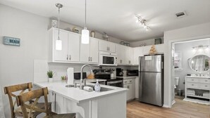 A modern kitchen with white cabinets, stainless steel appliances, and a wooden dining table.