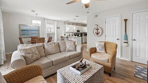 A living room with a beige sofa, a wicker armchair, a patterned coffee table, and a ceiling fan.