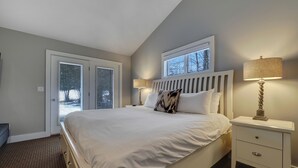 Une chambre avec un grand lit, une table de chevet avec une lampe, une fenêtre et une porte donnant sur l’extérieur.