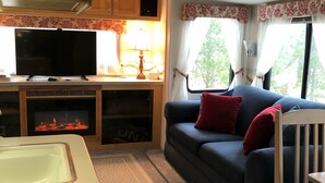 Een gezellig RV-interieur met een kitchenette, een televisie, een bank met rode kussens en een haard.