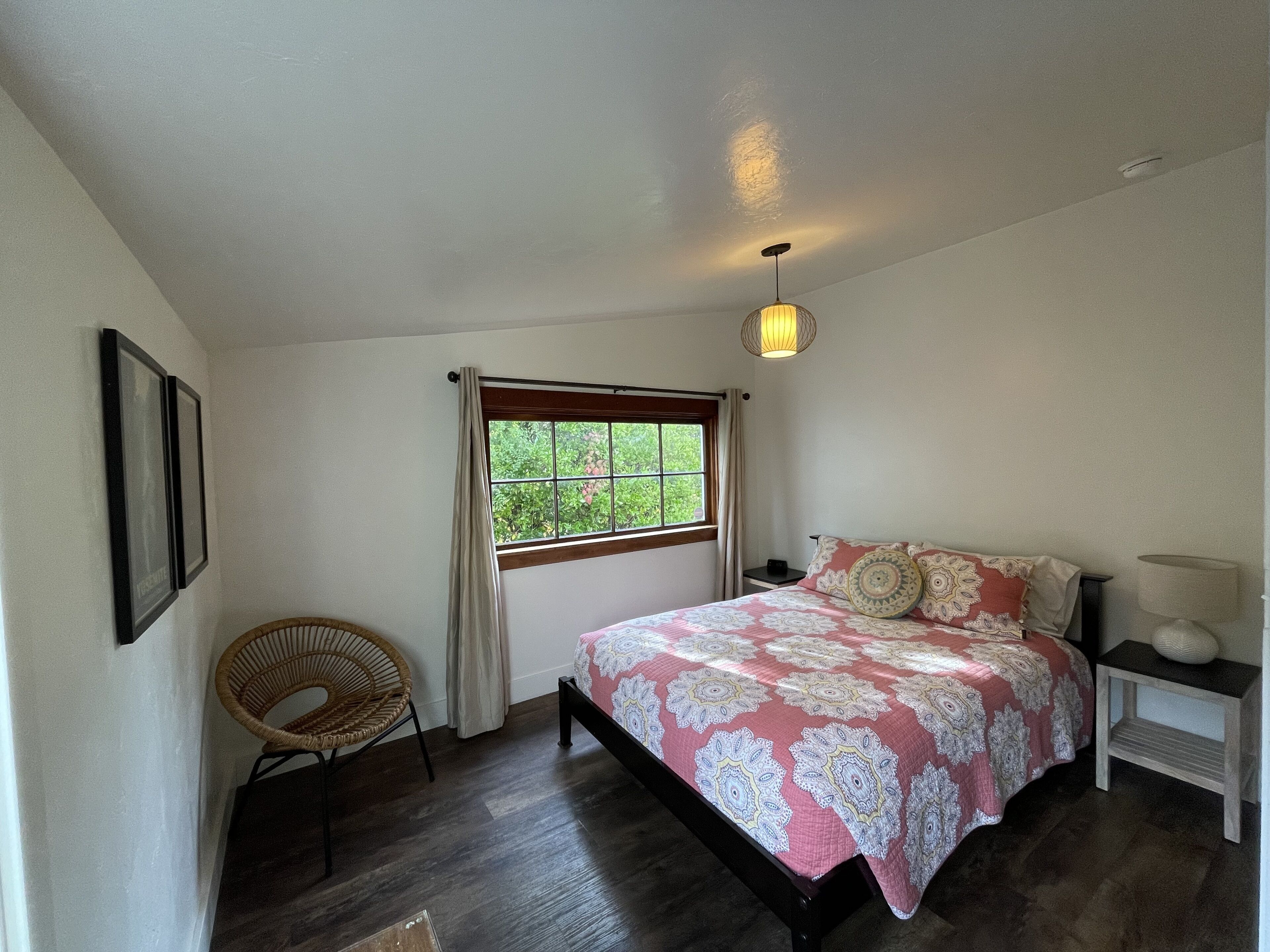Ein Schlafzimmer mit Bett, Fenster, Sessel, Nachttisch und einer Pendelleuchte.