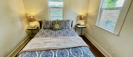 A bedroom with a bed, two bedside tables with lamps, a window, and a door.