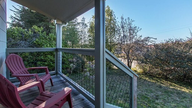 Un porche cubierto con dos sillas Adirondack y vistas a un jardín y árboles.