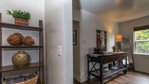 Una habitación con piso de madera, una consola de madera oscura con cajones, una planta en maceta y un florero en un estante.