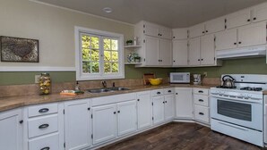 Una cocina con gabinetes blancos, microondas, horno, lavamanos y ventana con vistas a zonas verdes.