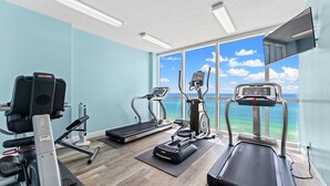 Un gimnasio con cintas de correr, elípticas y una bicicleta estática, con un amplio ventanal que ofrece vistas al océano.