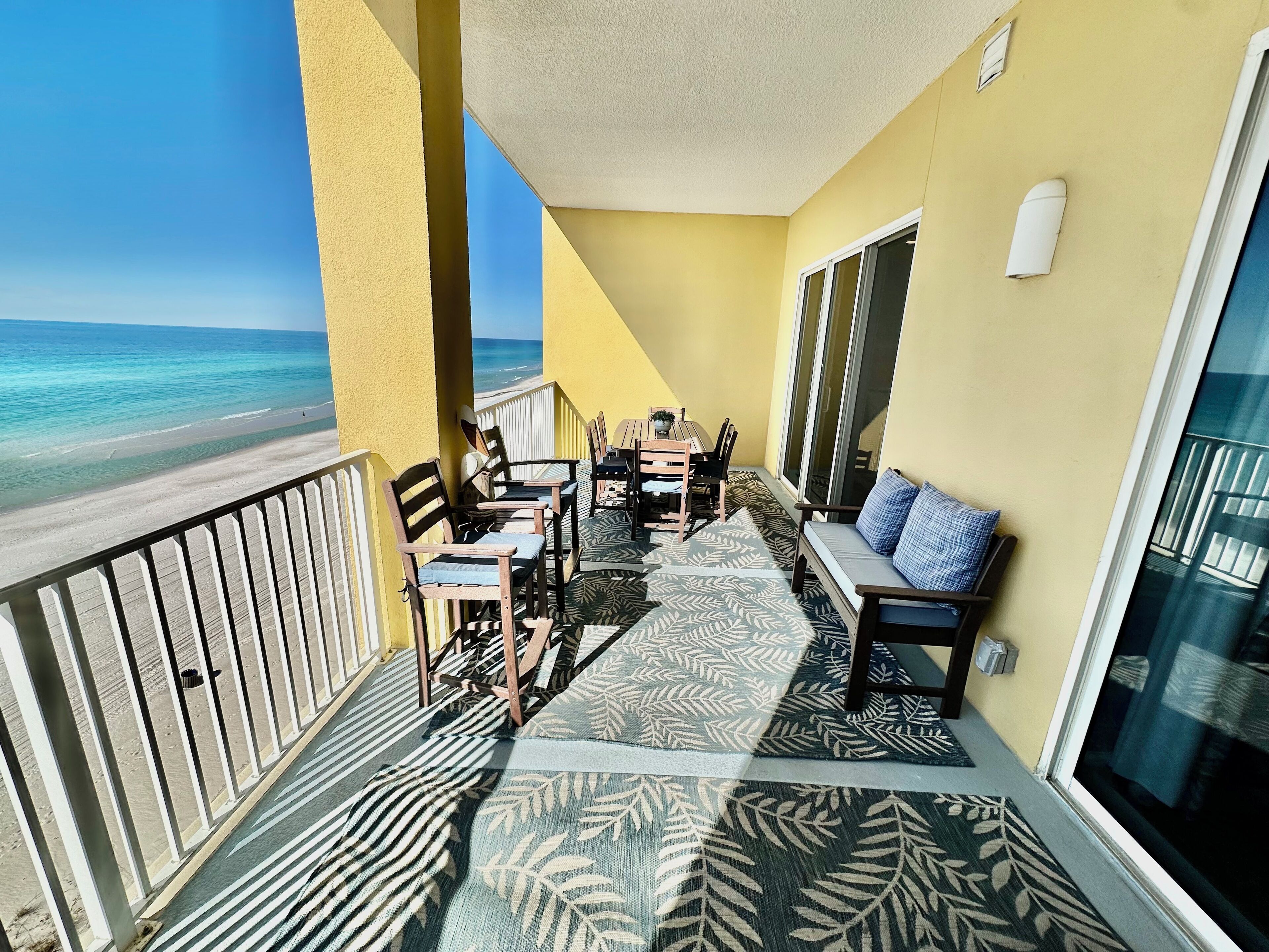 Een balkon met uitzicht op het strand, houten meubels en een tapijt met een patroon.