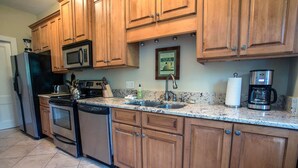 Una cocina con gabinetes de madera, electrodomésticos de acero inoxidable, encimera de granito y un cuadro en la pared.