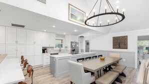 A modern kitchen with white cabinetry, a large island, and a dining area with a wooden table and chairs.