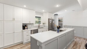 A modern kitchen with white cabinetry, a large island, stainless steel appliances, and a window providing natural light.