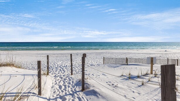 A sandy beach with a wooden fence and a clear view of the ocean.