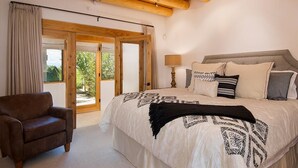 A bedroom with a bed, a chair, a lamp, and a view through a glass door. - Hacienda Artist Paradise (Santa Fe)