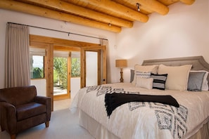 A bedroom with a bed, a chair, a lamp, and a view through a glass door.