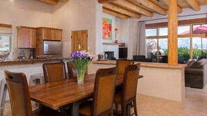 A kitchen with wooden cabinets, a dining table with chairs, a refrigerator, and a vase with flowers. - Hacienda Artist Paradise (Santa Fe)