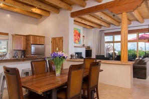 A kitchen with wooden cabinets, a dining table with chairs, a refrigerator, and a vase with flowers.
