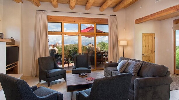 A spacious living room with a large window, wooden ceiling beams, and a cozy seating area. - Hacienda Artist Paradise (Santa Fe)